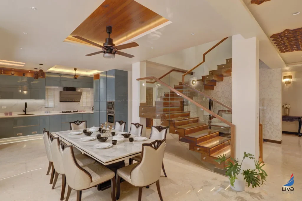 Modern open-plan dining and kitchen space by an interior designing company in India with wooden staircase, modular kitchen, and false ceiling lighting